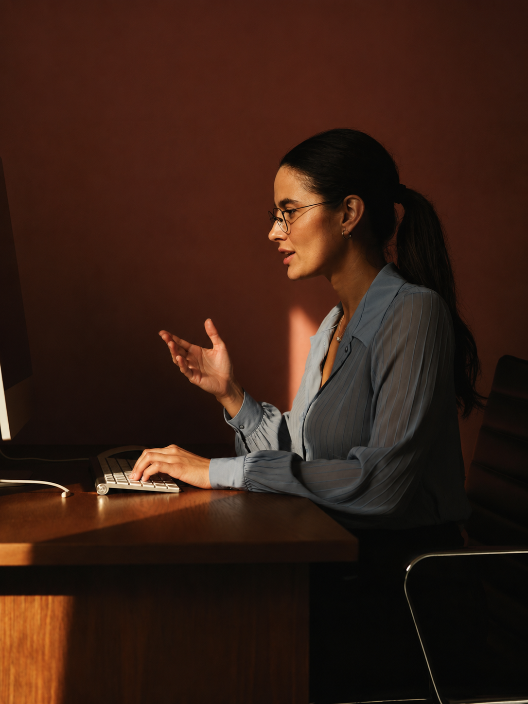 A woman typing at a white keyboard against a deep terracotta wall